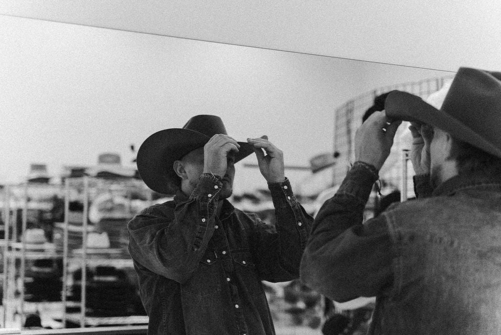 A black and white grainy image of Parker wearing and shaping a custom cowboy hat