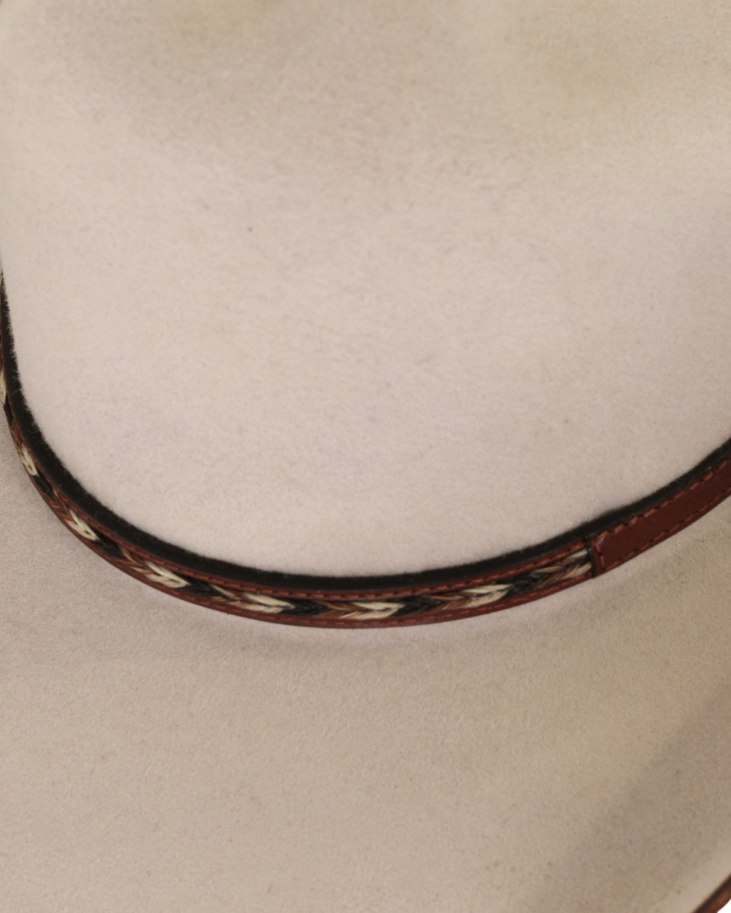 Close-up detailed view of a silverbelly dallas cattleman cowboy hat with a horse hair multicolored leather hat band and silver buckle with minimal brim edge burning 

