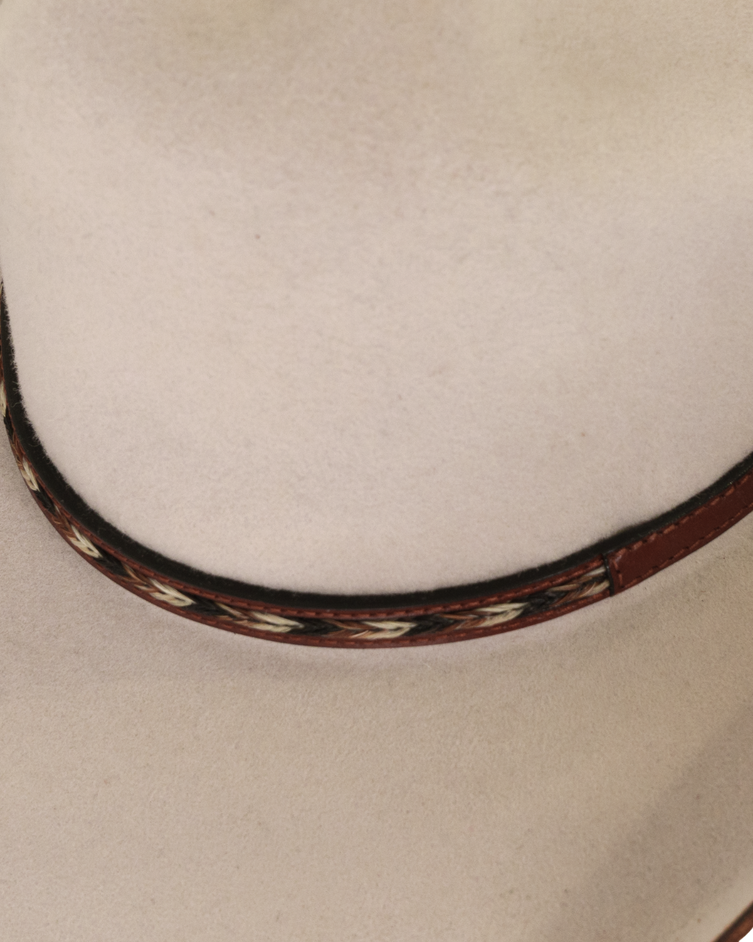 Close-up detailed view of a silverbelly dallas cattleman cowboy hat with a horse hair multicolored leather hat band and silver buckle with minimal brim edge burning 
