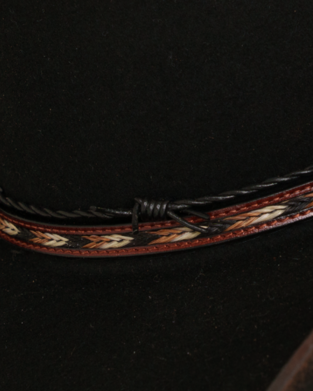 Close-up view of a black Dallas Cattleman cowboy hat with a multicolor horsehair braided and leather hat band, silver buckle, a black barbed-wire style accent band
